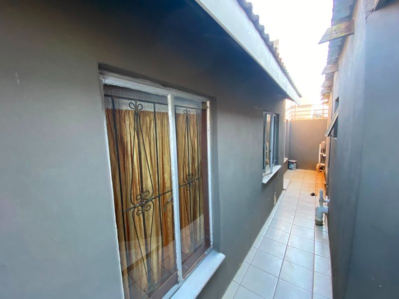 A narrow exterior side passage featuring tiled flooring, security bars on windows, and painted exterior walls.