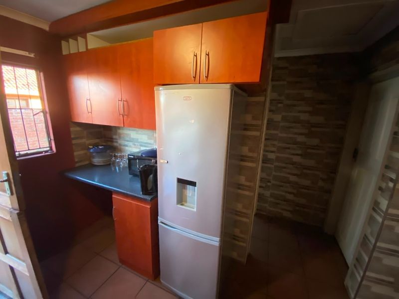 A compact kitchen featuring wood-tone cabinetry, stone-look tile backsplash, and tiled flooring, offering a functional layout with integrated storage space.