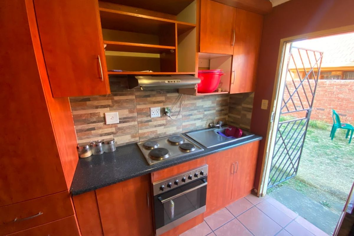 Compact kitchen featuring wooden cabinetry, built-in electric oven and hob, tiled backsplash, and direct access to the rear garden area.