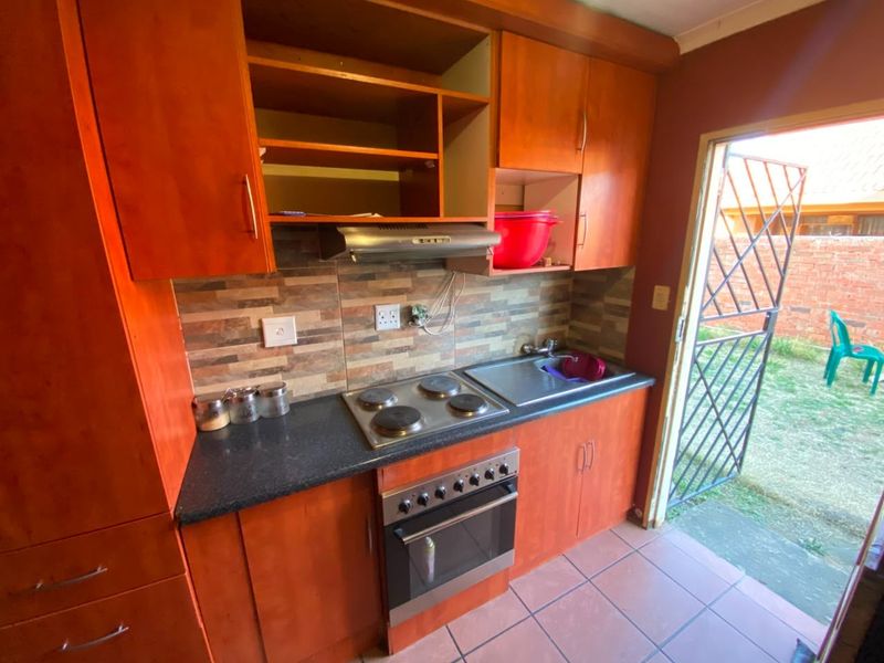 Compact kitchen featuring wooden cabinetry, built-in electric oven and hob, tiled backsplash, and direct access to the rear garden area.