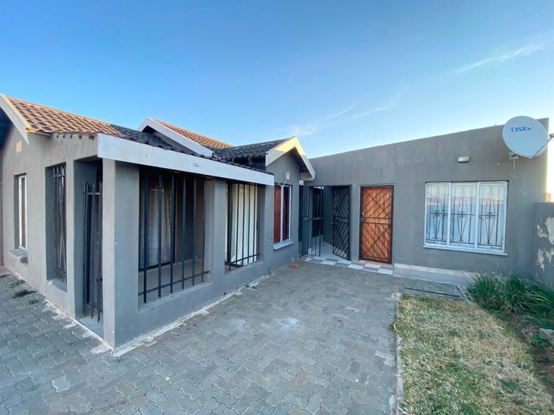 Rear exterior view of the house featuring a paved patio area, security bars on windows, and a tiled roof structure.
