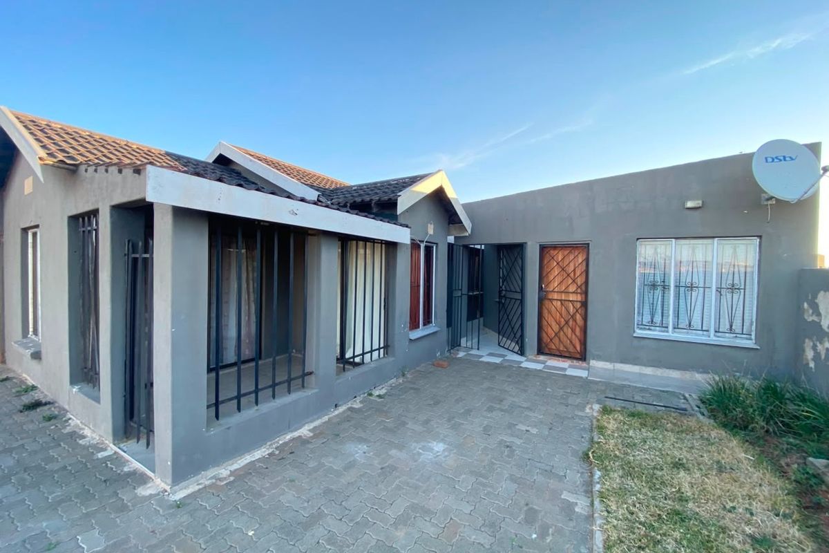 Rear exterior view of the house featuring a paved patio area, security bars on windows, and a tiled roof structure.