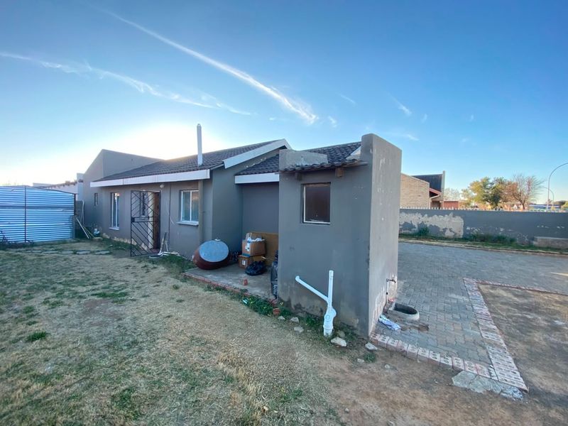 Rear view of the house featuring a paved area, security gate, and boundary wall with visible maintenance required on exterior finishes.
