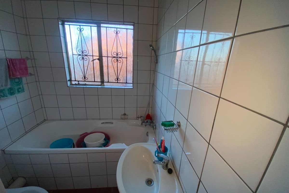 A functional bathroom featuring a bathtub, pedestal basin, toilet, and full-height ceramic wall tiling with a window for natural light.