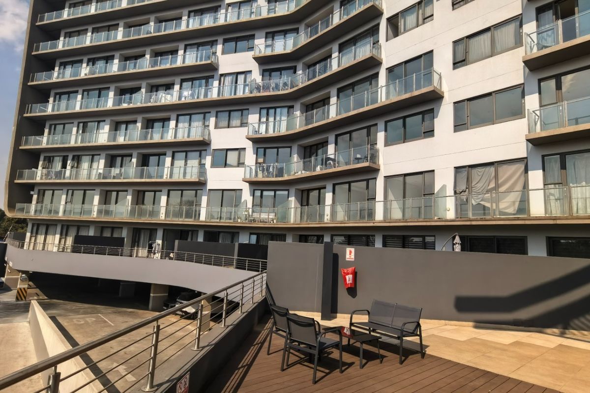 A view of the multi-story penthouse building facade featuring private balconies with glass balustrades and a paved outdoor terrace area.