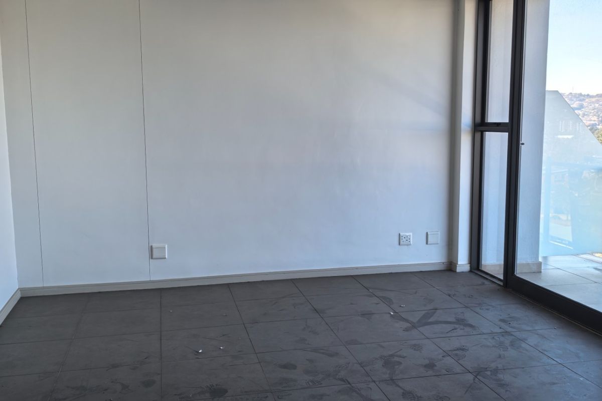 An empty living room featuring large glass sliding doors leading to a balcony, with tiled flooring and neutral walls.
