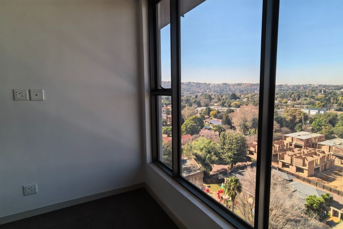 A bright, empty bedroom featuring large floor-to-ceiling windows that offer expansive views of the surrounding neighborhood and landscape.