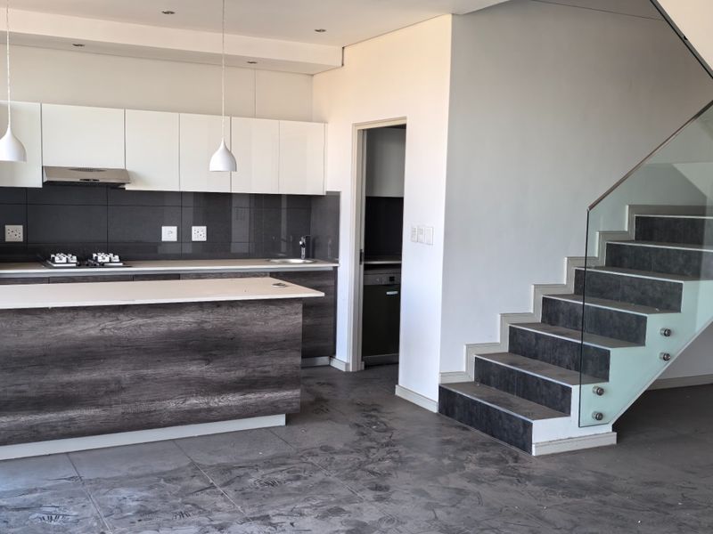 Modern open-plan kitchen featuring dark wood cabinetry, a central island, and a sleek staircase with a glass balustrade in a contemporary penthouse setting.