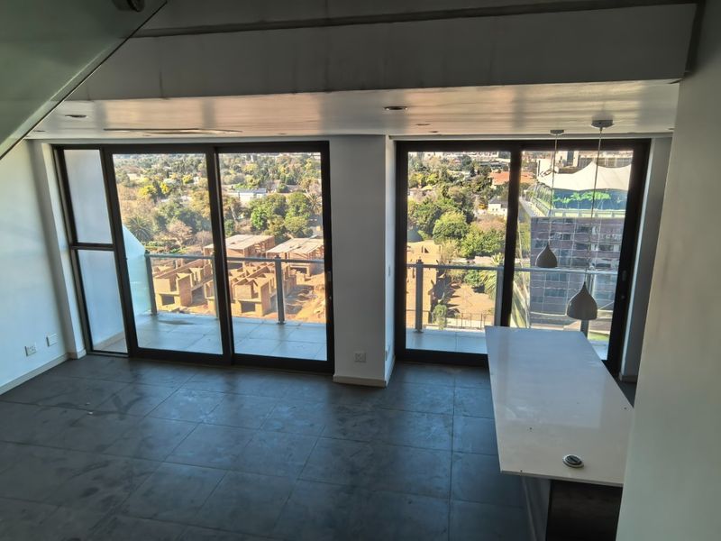 Spacious open-plan penthouse area featuring a stone island, modern glass balustrade, and large sliding doors opening to a balcony with expansive urban views.
