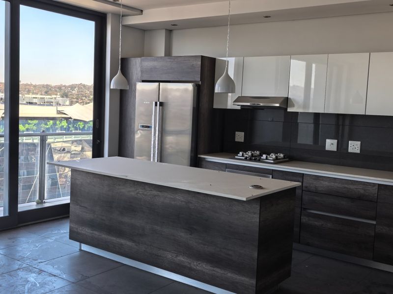 Modern kitchen featuring dark wood cabinetry, a central island, integrated appliances, and large sliding doors opening to a balcony with city views.