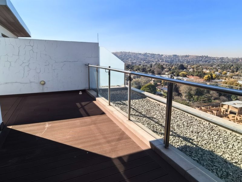Spacious penthouse balcony featuring composite decking, a modern glass balustrade with stainless steel handrail, and expansive elevated views.