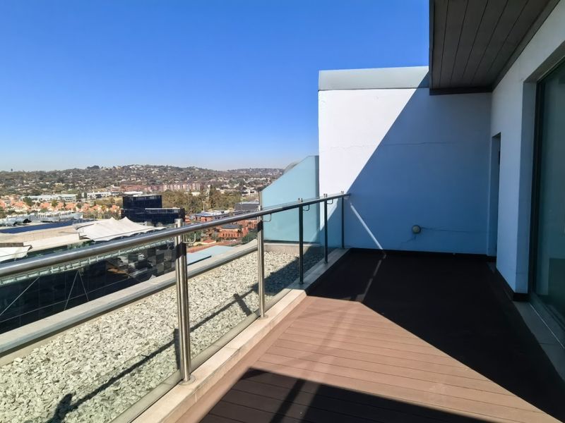 A spacious penthouse balcony featuring composite decking, a modern stainless steel and glass balustrade, and expansive urban views.