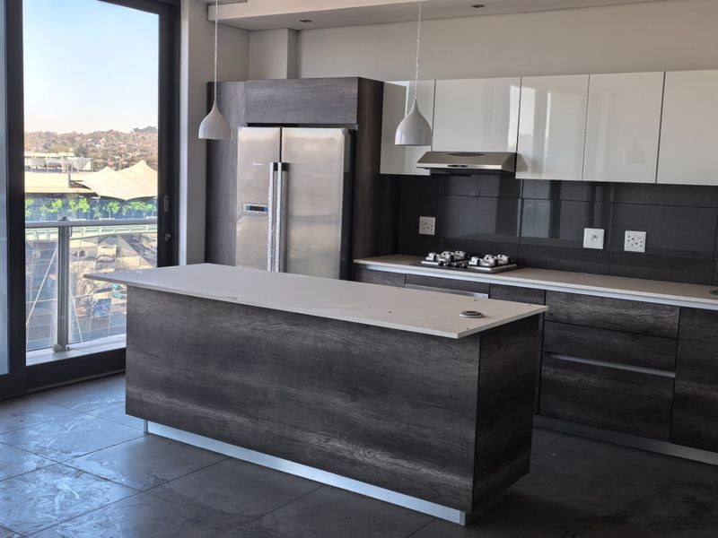 Modern kitchen featuring dark wood and white cabinetry, stone countertops, a central island, and integrated appliances with access to a balcony.