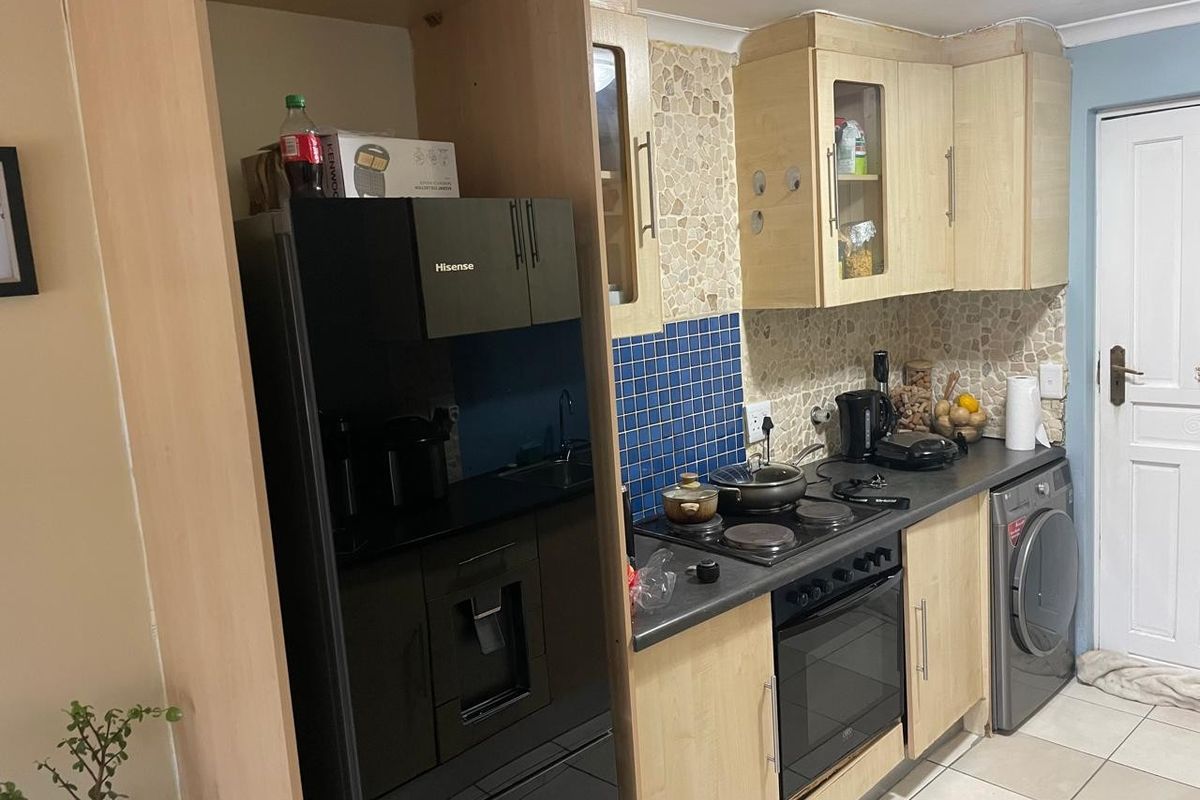 Compact kitchen featuring light wood cabinetry, dark laminate countertops, electric hob, built-in oven, and integrated laundry appliance with a tiled backsplash.
