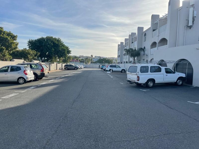 Exterior view of the apartment complex parking area featuring paved parking bays and perimeter security fencing.