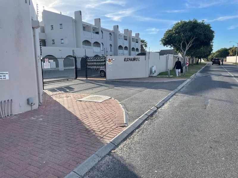 Street view of the apartment complex entrance featuring a secure gated access point, boundary wall, and paved driveway.