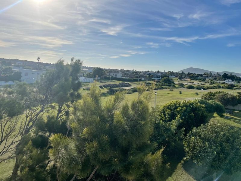 A scenic elevated view overlooking a green landscape with surrounding residential properties and distant hills.