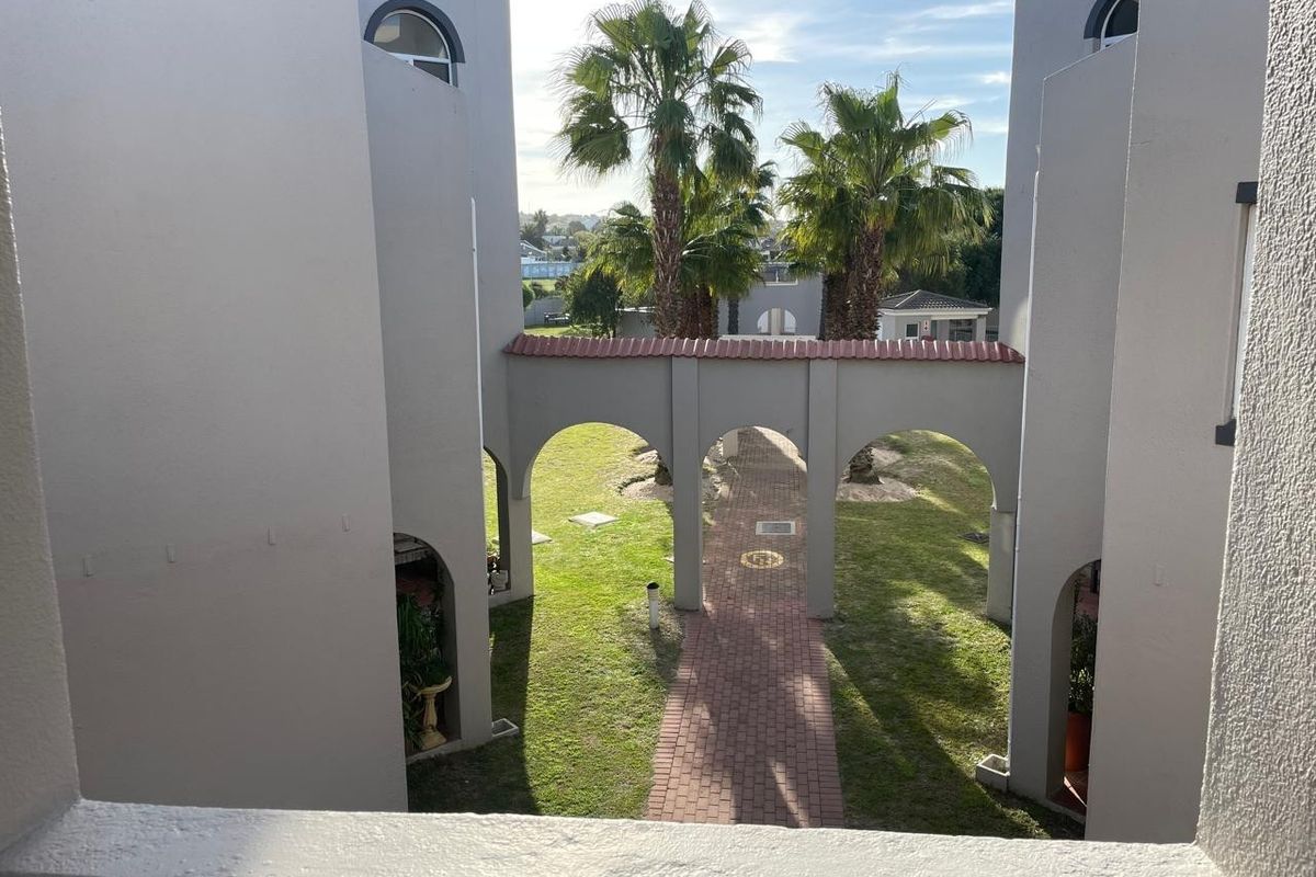 View of a landscaped courtyard featuring a brick paved walkway and arched architectural elements between apartment building wings.