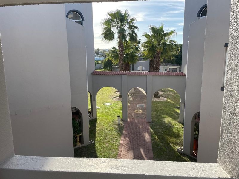 View of a landscaped courtyard featuring a brick paved walkway and arched architectural elements between apartment building wings.