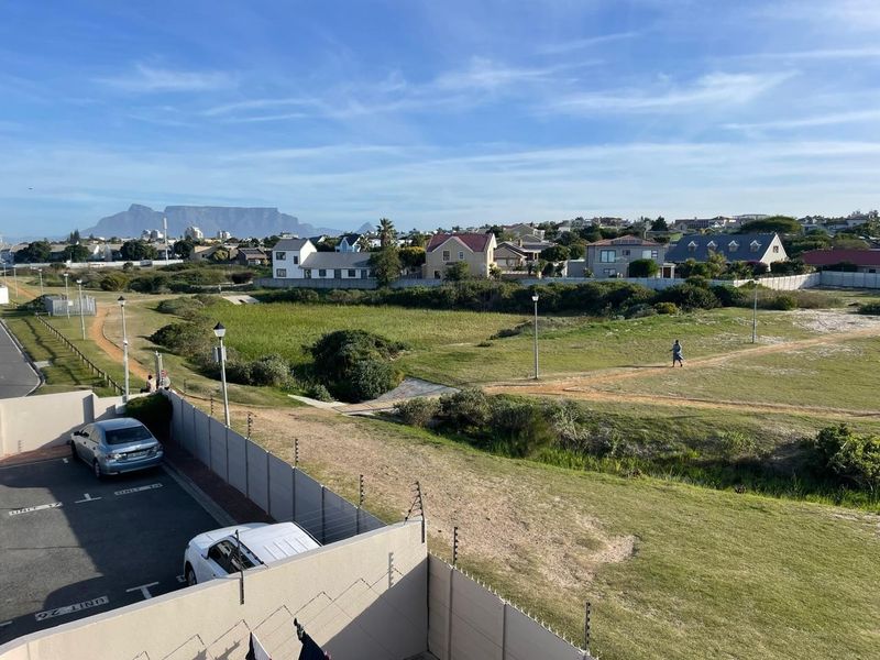Elevated view overlooking a green belt area with Table Mountain in the distance, featuring secure boundary walling and electric fencing.