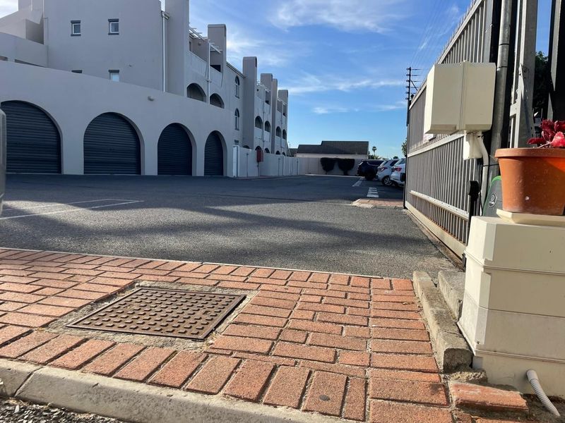 Exterior view of the apartment complex entrance, featuring a paved driveway, secure metal gate, and multiple garage units.