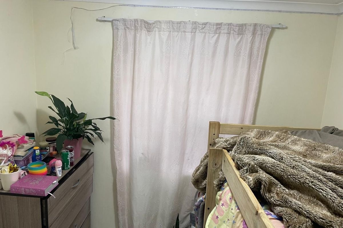 A bedroom featuring a window with a curtain rod and decorative coving, showing signs of wear including exposed surface wiring.