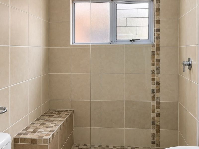 A clean, modern bathroom featuring a spacious walk-in shower with a built-in tiled bench, glass screen, and neutral ceramic tiling throughout.