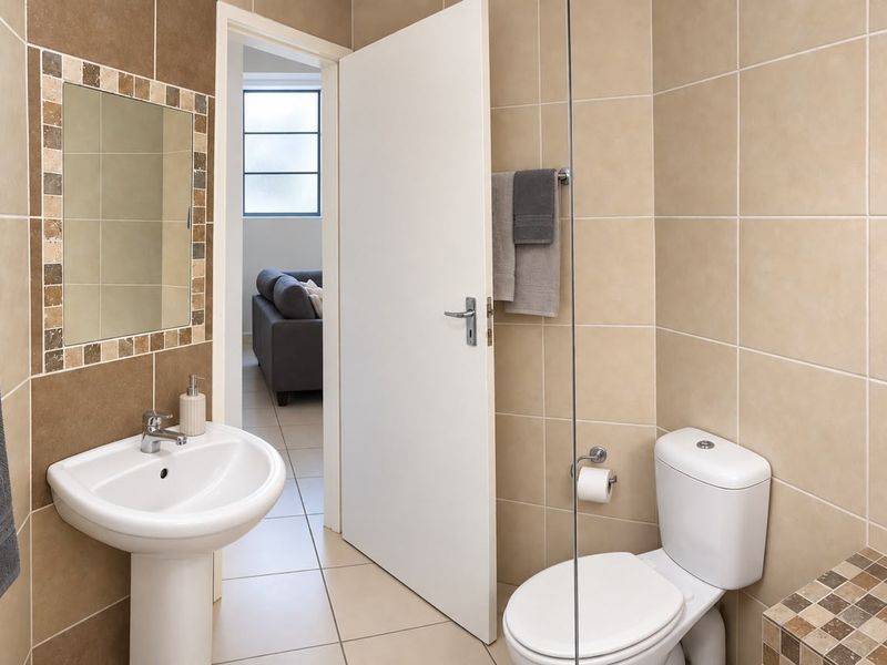 A clean, well-maintained bathroom featuring a pedestal washbasin, toilet, and a glass shower screen with neutral-toned wall and floor tiling.