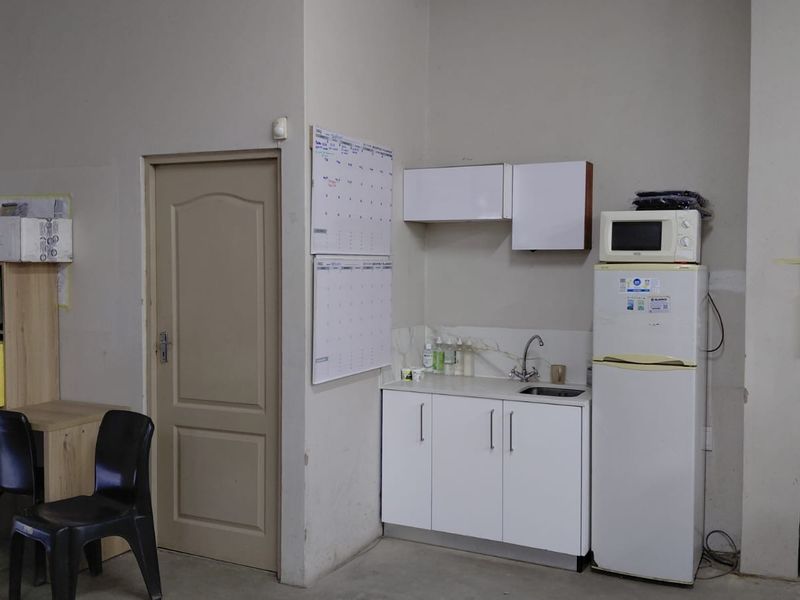 A functional industrial scullery or kitchenette area featuring white built-in cabinetry, a sink, and wall-mounted storage units.