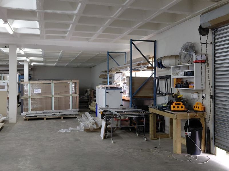 Spacious industrial workshop area featuring a waffle slab ceiling, concrete flooring, and a large roller shutter door for easy access.