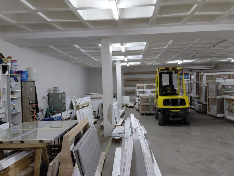 Spacious industrial warehouse area featuring a waffle slab ceiling, concrete flooring, and functional overhead lighting, currently utilized for storage and logistics.