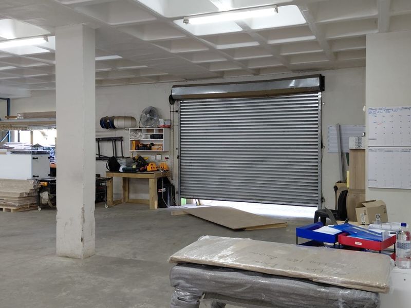 Spacious industrial utility area featuring a high-clearance roller shutter door, exposed waffle slab ceiling, and durable concrete flooring, suitable for workshop or storage use.