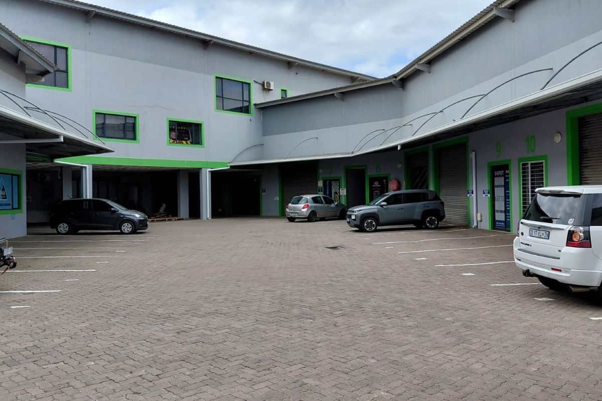 Industrial complex exterior featuring a paved courtyard with multiple roller shutter access points and designated parking bays.