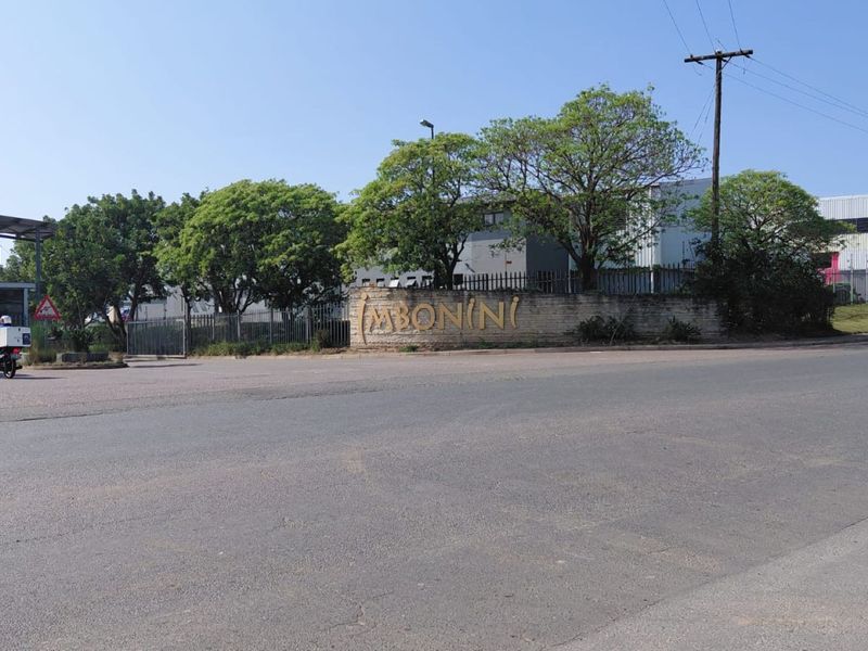 Street view of the industrial property entrance featuring a security gate, perimeter fencing, and prominent signage.