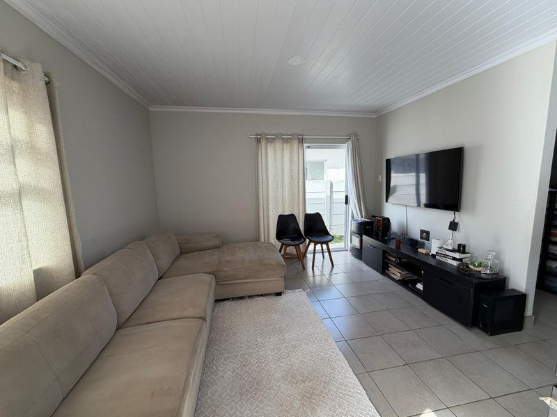 A well-maintained living room featuring tiled flooring, a tongue and groove ceiling, and a sliding glass door providing access to the exterior.