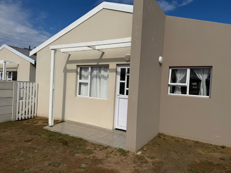 Rear exterior view of the townhouse featuring a small tiled patio, a timber pergola, and low-maintenance garden space.