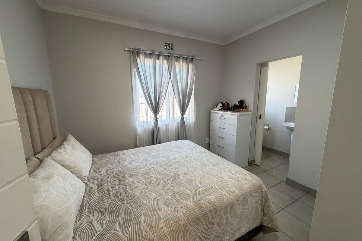 A functional bedroom featuring tiled flooring and an adjoining en-suite bathroom, providing a neutral and practical living space.