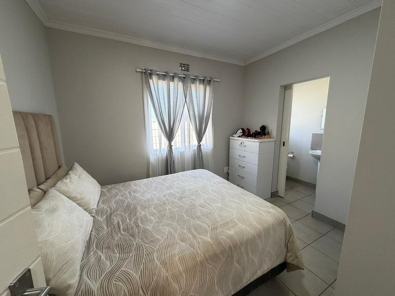 A functional bedroom featuring tiled flooring and an adjoining en-suite bathroom, providing a neutral and practical living space.