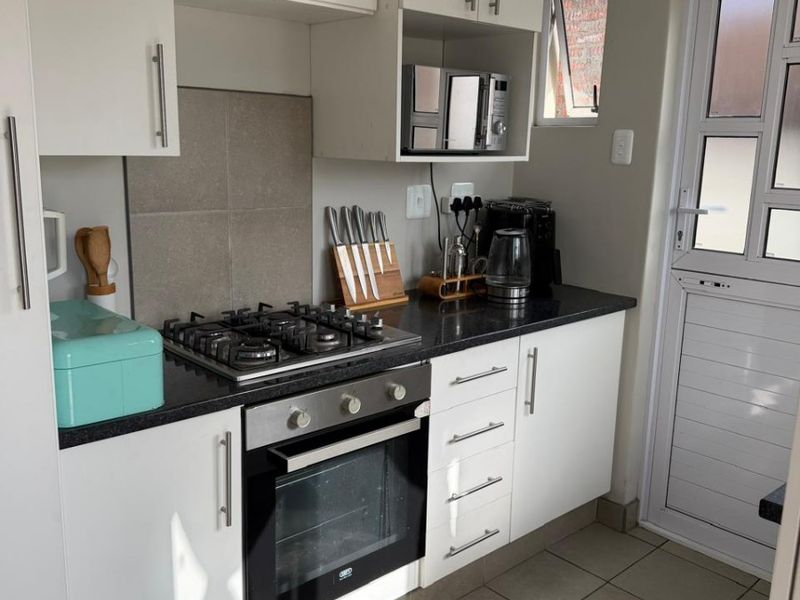 Compact kitchen featuring white cabinetry, granite countertops, a gas hob, built-in oven, and tiled flooring with direct access to an exterior door.