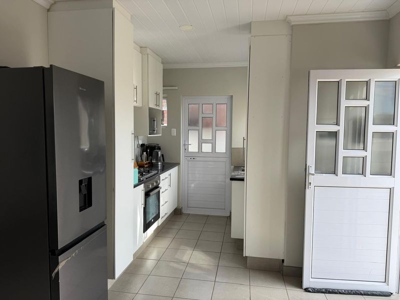 A functional kitchen featuring white cabinetry, tiled flooring, built-in oven and hob, and direct access to the exterior.