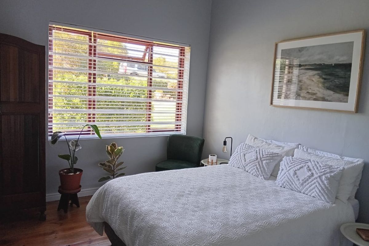 A well-lit bedroom featuring polished timber flooring and a large window with venetian blinds, offering a comfortable and inviting living space.