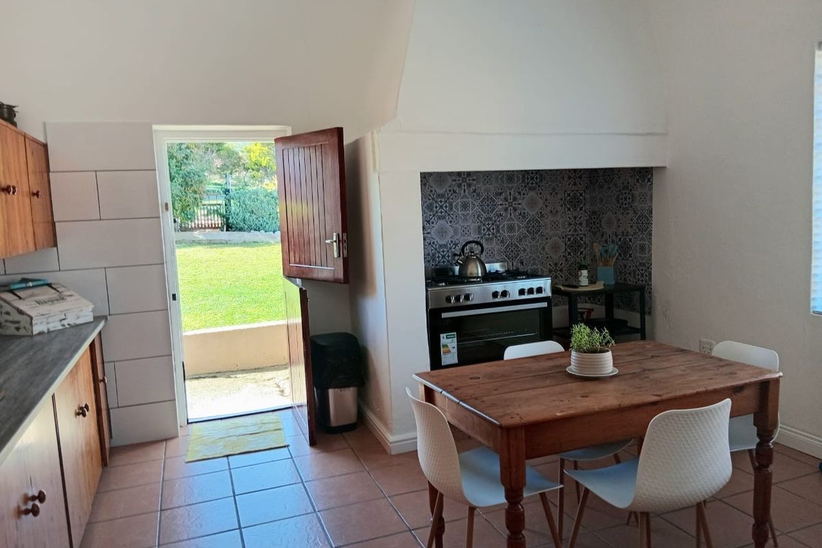 A rustic kitchen featuring a built-in oven with a decorative tiled splashback, wooden cabinetry, tiled flooring, and direct access to the garden via a stable door.