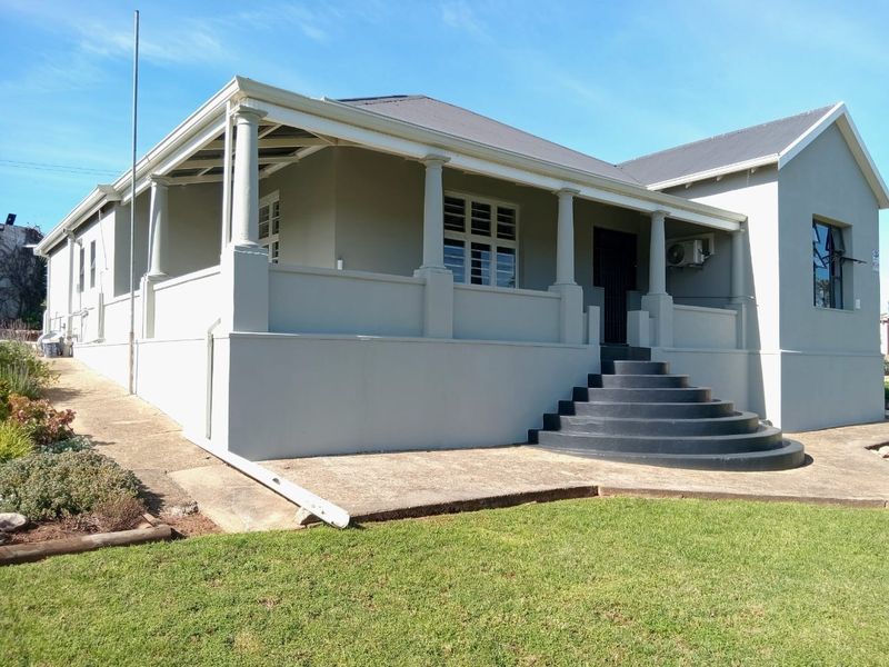Front elevation of a house featuring a covered veranda with columns, concrete stairs, and a well-maintained lawn area.