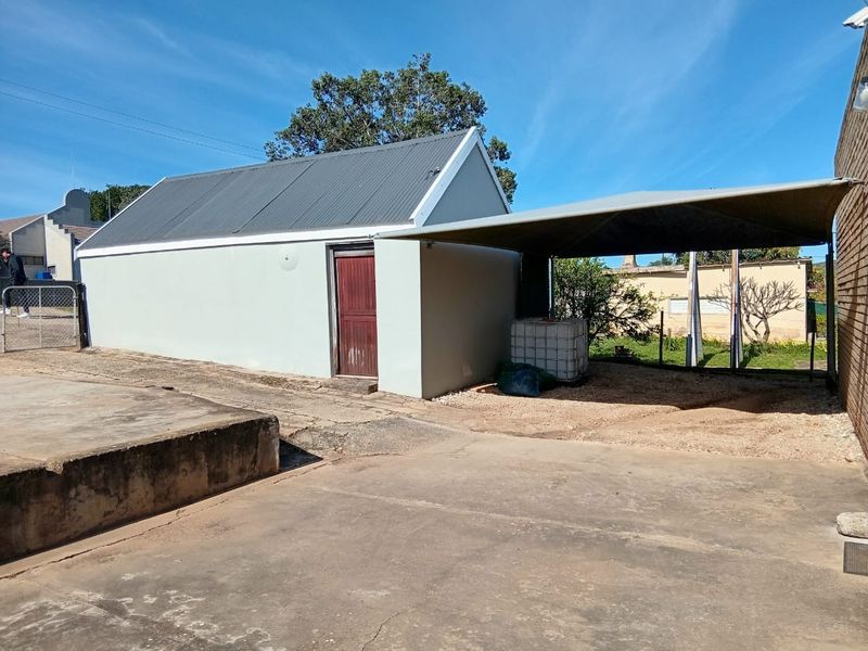 Rear exterior view showing a detached outbuilding with a corrugated metal roof and an attached shade cloth carport over a concrete driveway.