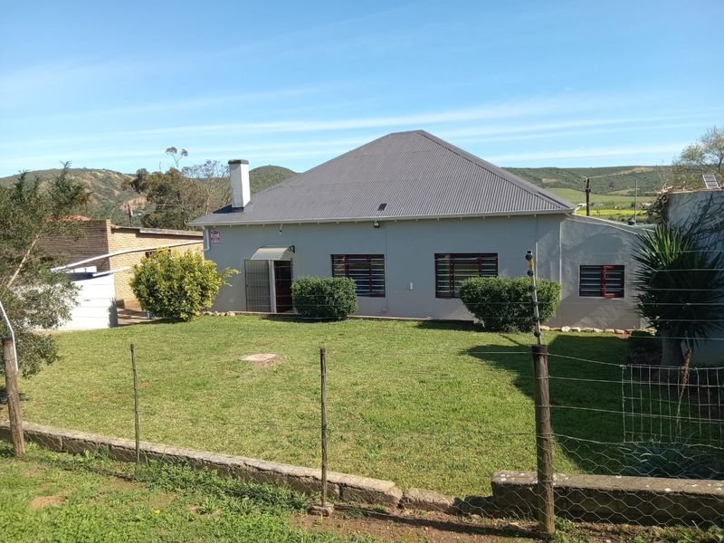 Rear view of a detached house featuring a corrugated metal roof, brick chimney, and a spacious lawn area enclosed by wire fencing.
