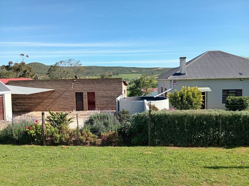 Rear view of the property featuring a brick outbuilding, water tank, and well-maintained garden with scenic mountain views in the background.
