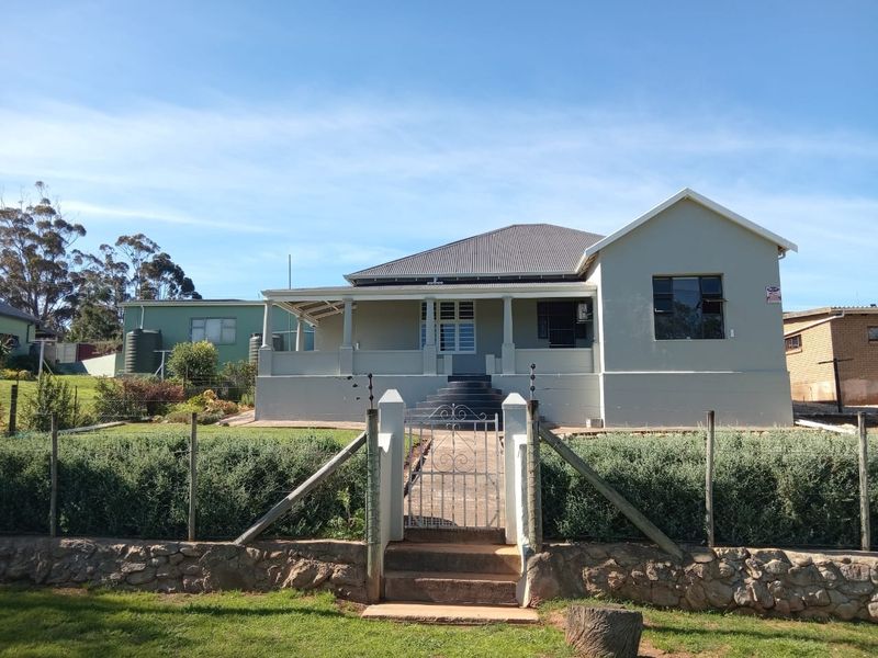Front view of a well-maintained house featuring a covered veranda, stone retaining wall, and secure gated entrance with electric fencing.