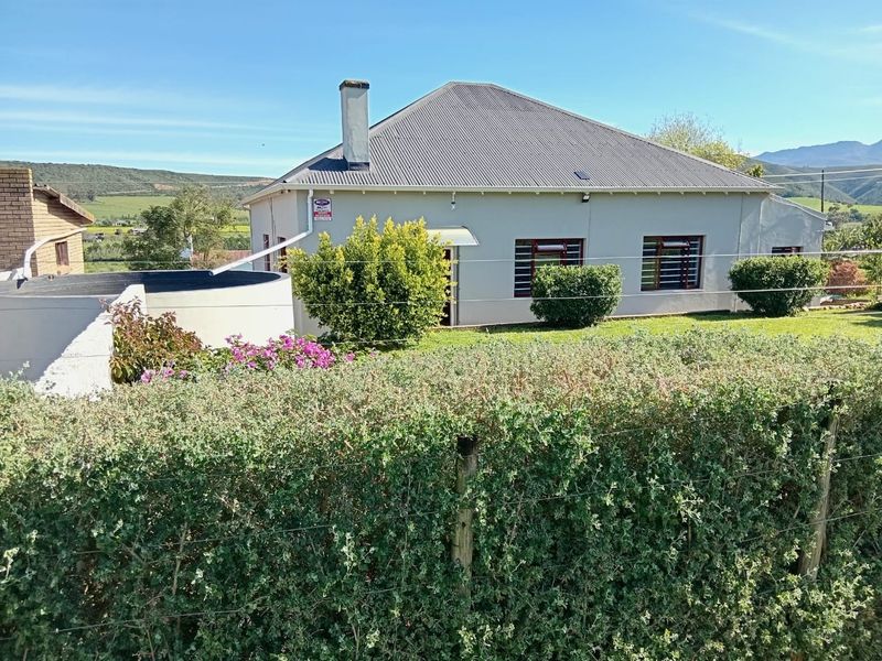 Rear view of the property featuring a corrugated metal roof, masonry chimney, and a well-maintained garden with a water tank.