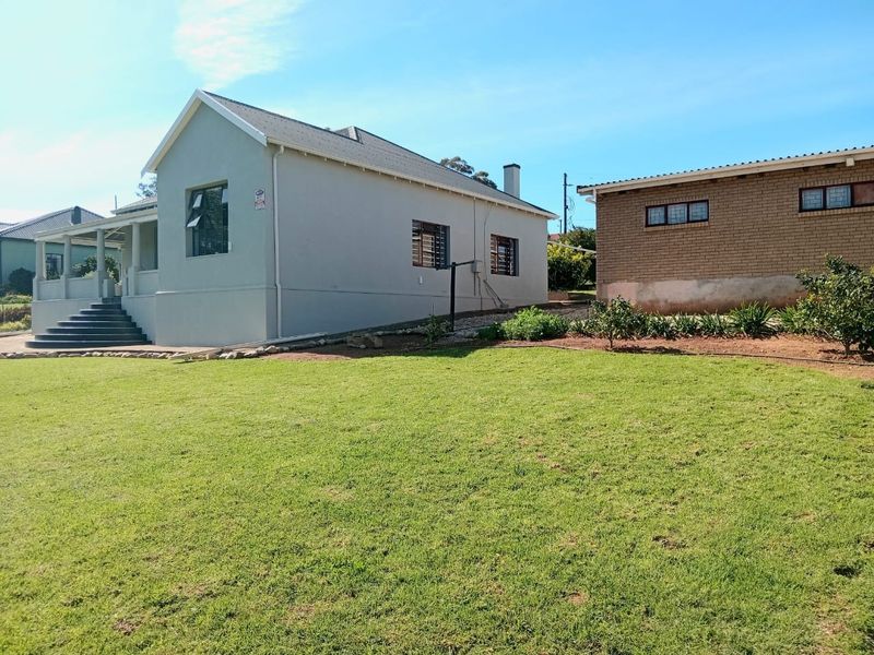 A view of the rear exterior featuring a well-maintained lawn, a main house with a covered porch, and a separate brick outbuilding.