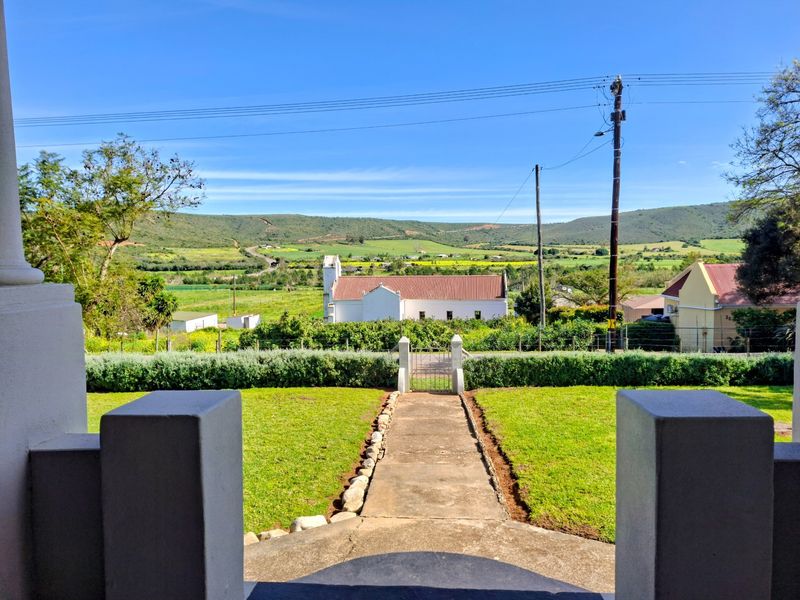 A scenic view from the property overlooking a rural landscape, featuring a well-maintained lawn, concrete pathway, and a metal gate.